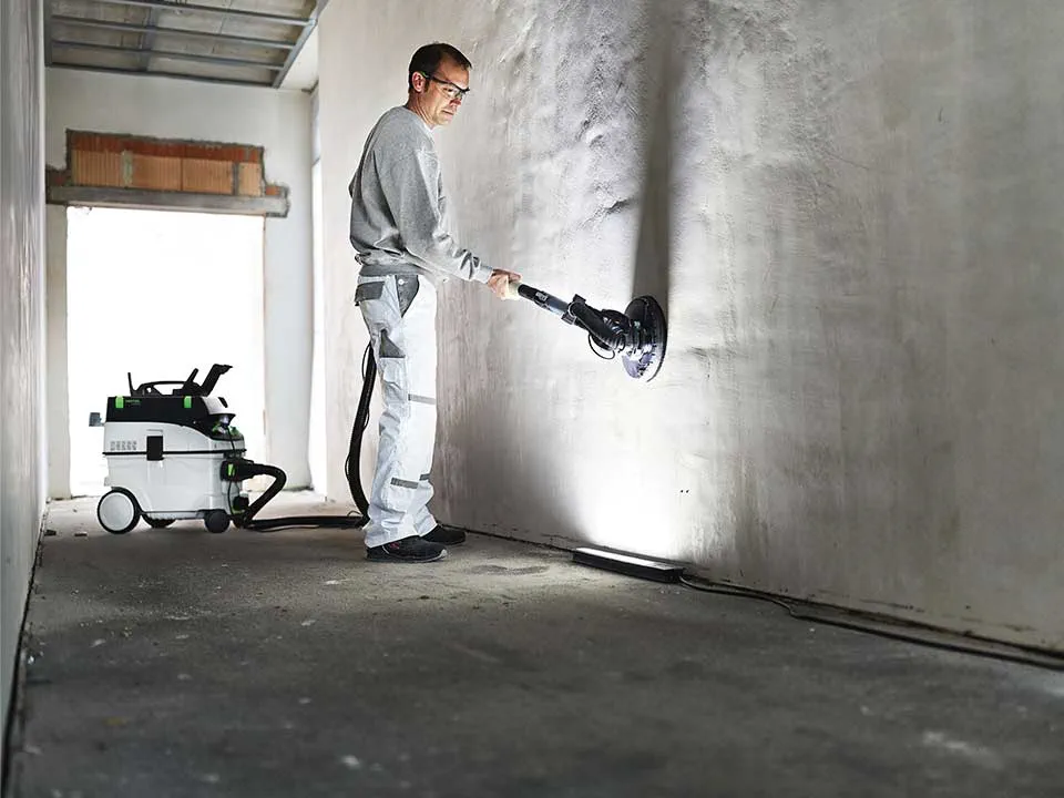 Занаятчия осветява стена с помощта на Контролната лампа и я шлайфа.